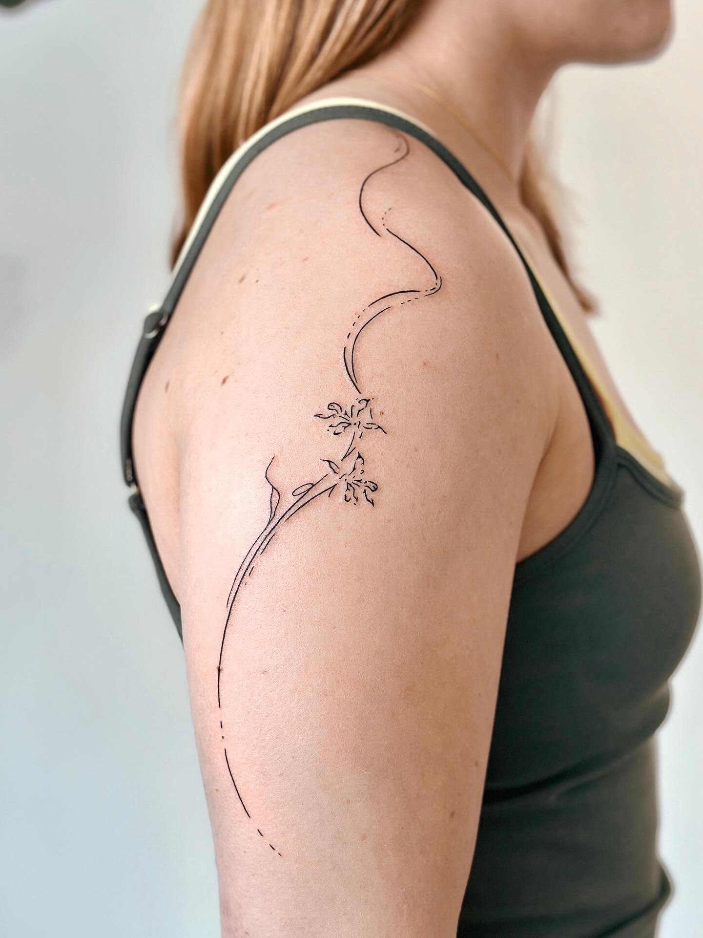 Long fine line floral tattoo flowing across the shoulder